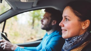 Usmievavý vodič sa pozerá na usmievavú spolujazdkyňu so slnečnými okuliarmi.