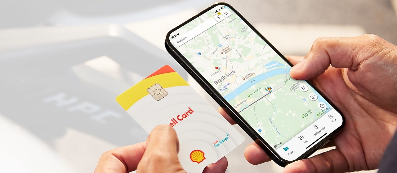Karta Shell v ruke a mobilný telefón s aplikáciou Recharge s navigáciou k najbližšej stanici.