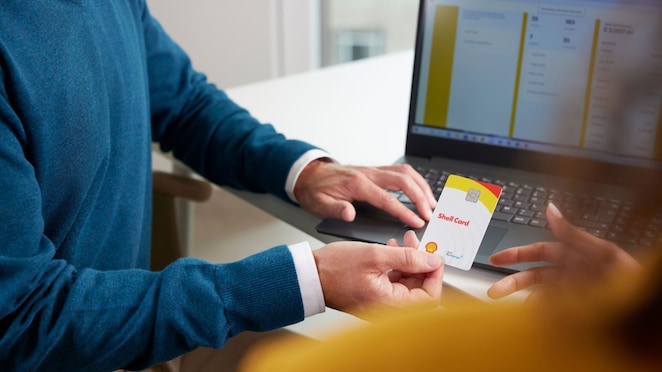 Detailný pohľad na muža, ktorý odovzdáva bielu čipovú kartu Shell Card žene v kancelárskom prostredí pred notebookom.