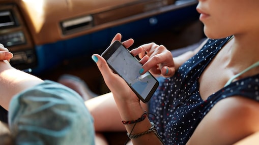 Foto muža a ženy v aute, ako sa dívajú na mapu v mobile