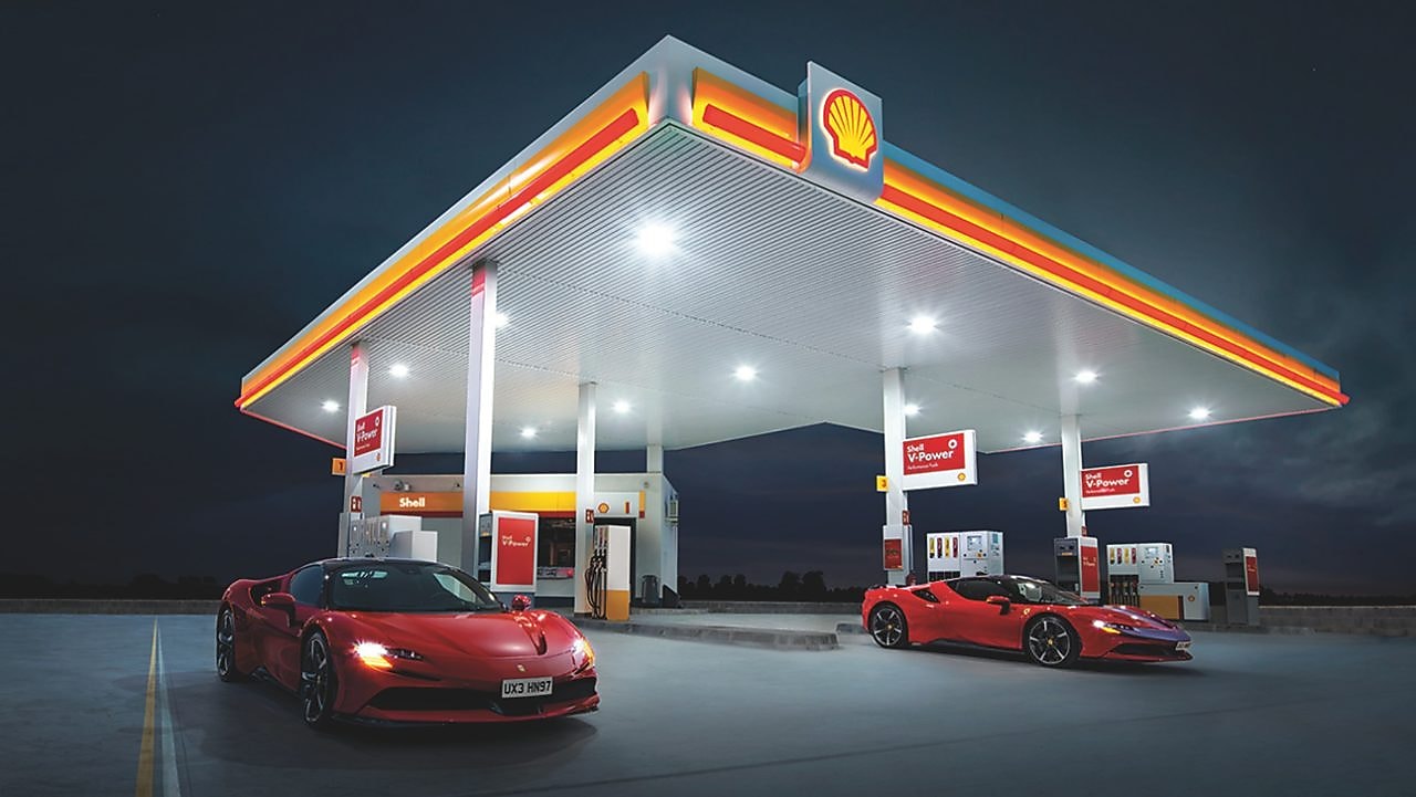 Obrázok čerpacej stanice Shell v noci s dvoma zaparkovanými vozidlami Ferrari.