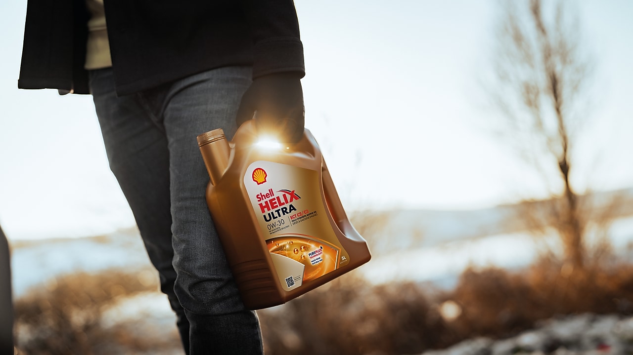 Ruka muža držiaca olej Shell Helix Ultra.