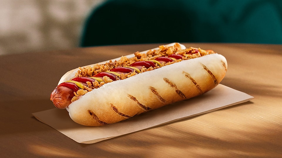 Na vizuáli možno vidieť vegetariánsku ponuku hotdogu s horčicou, kečupom a sušenou cibuľou.