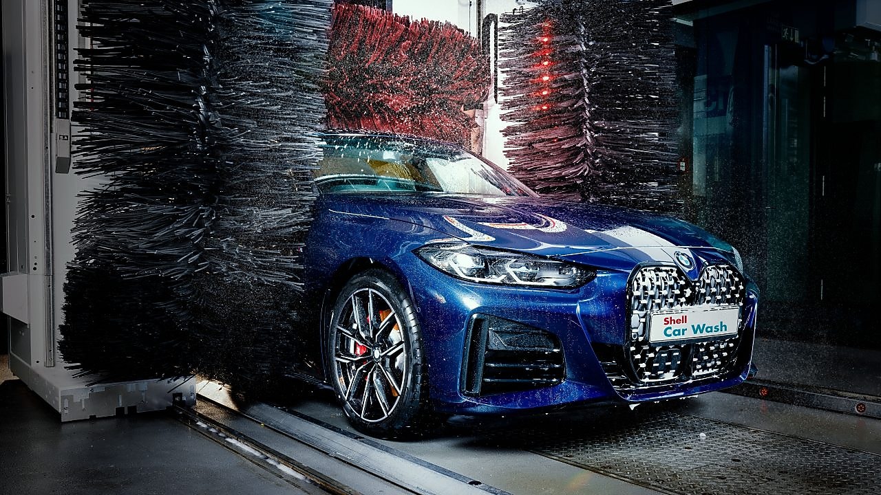 Modré auto v detailnom zábere prechádza cez Shell autoumyváreň.