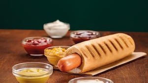 Foto hot dogu Klasik, na pozadí možno vidieť horčicu a kečup v sklenených mištičkách